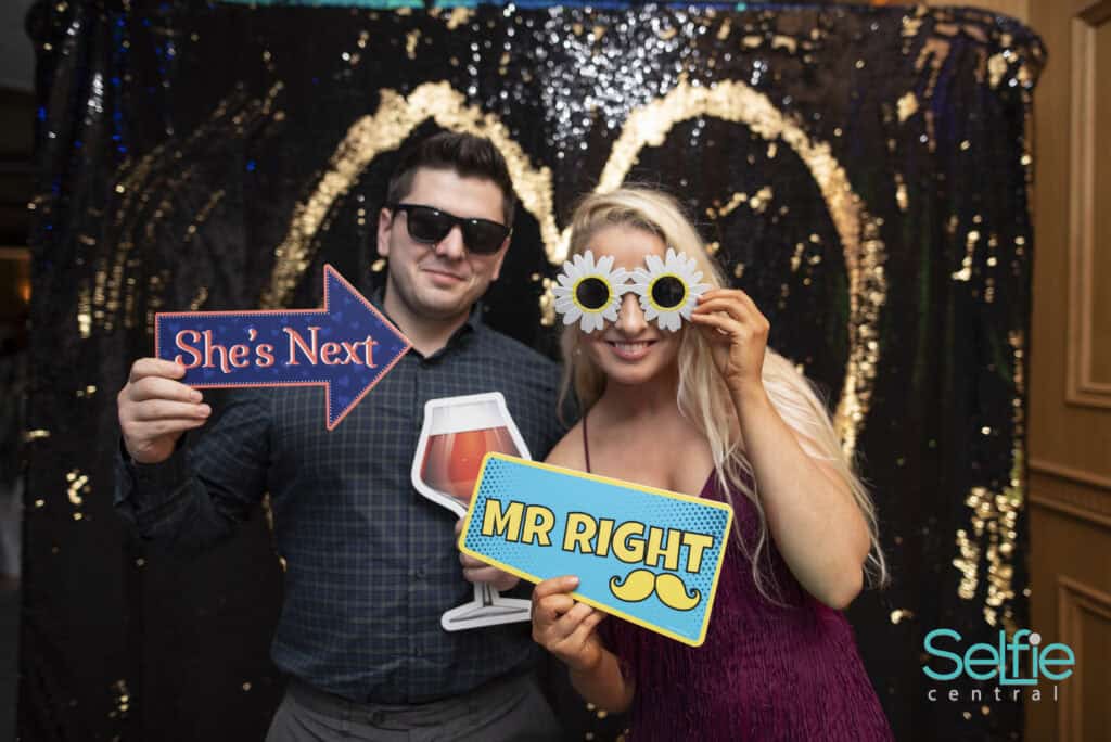 Happy couple enjoying photo booth at Auckland event with fun props and backdrop.