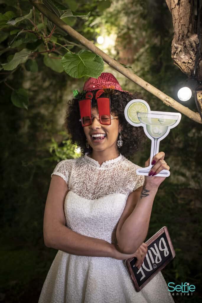 Woman with fun accessories holding a cocktail prop at a photo booth event in Auckland.