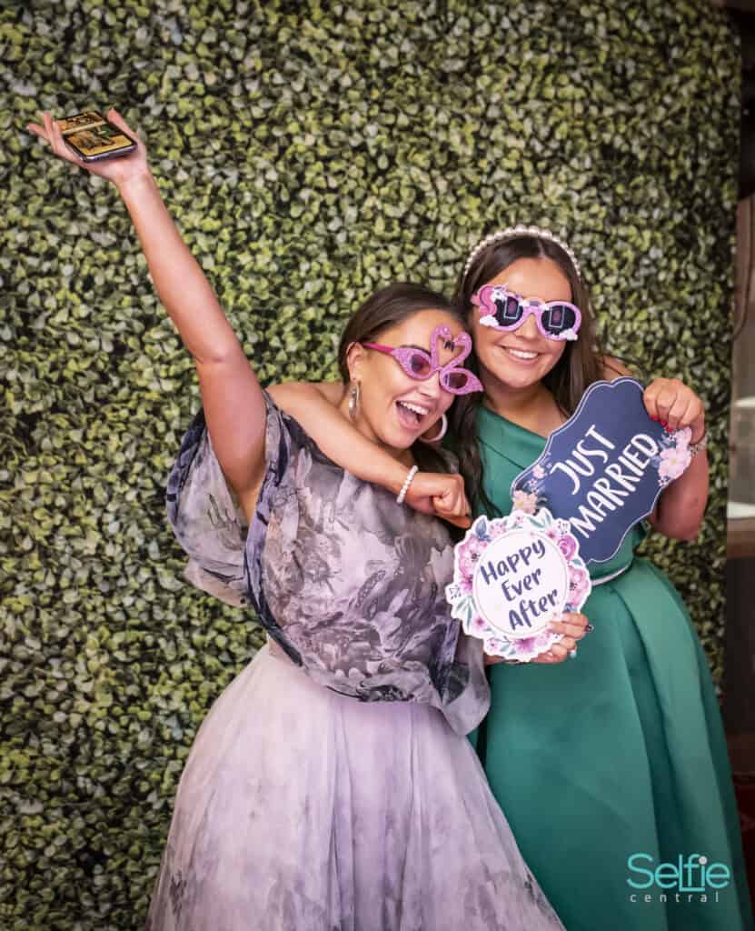 Two women at a photo booth with fun props and signs in Auckland.