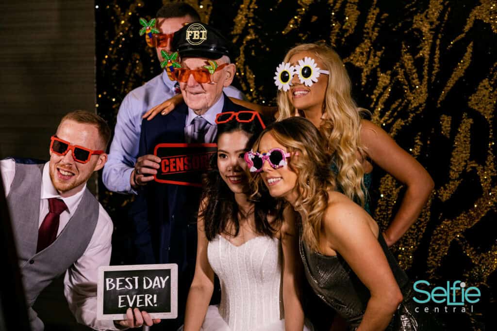 Group of friends and a senior man enjoying fun photo booth pictures at an event in Auckland.
