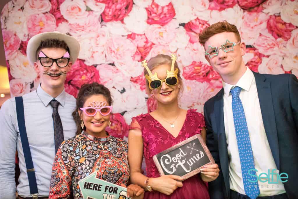Group of friends enjoying a photo booth at an event in Auckland with fun props and a floral backdrop.