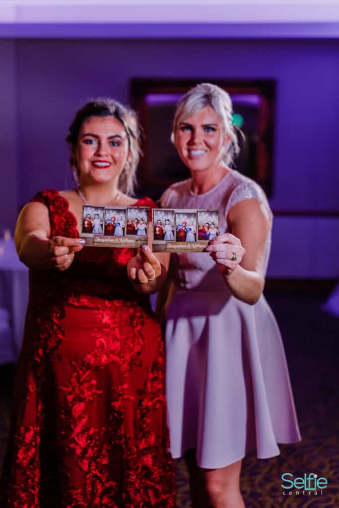 Two women holding photo booth strips at an Auckland event, smiling and enjoying the selfie experienc.