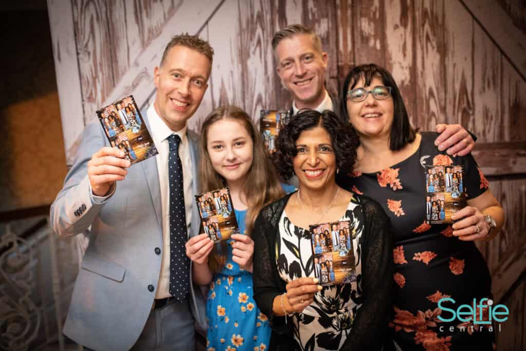 Group of people enjoying a photo booth at an Auckland event, smiling and holding printed photos.