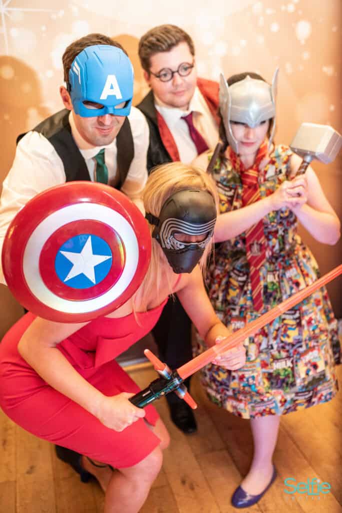 Group of people in superhero costumes at a photo booth, having fun and posing with props.