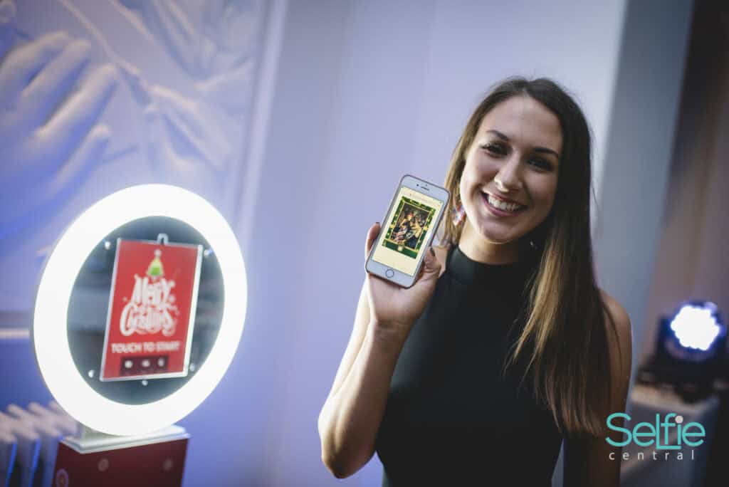 Smiling woman showing smartphone with photo booth at Auckland event.
