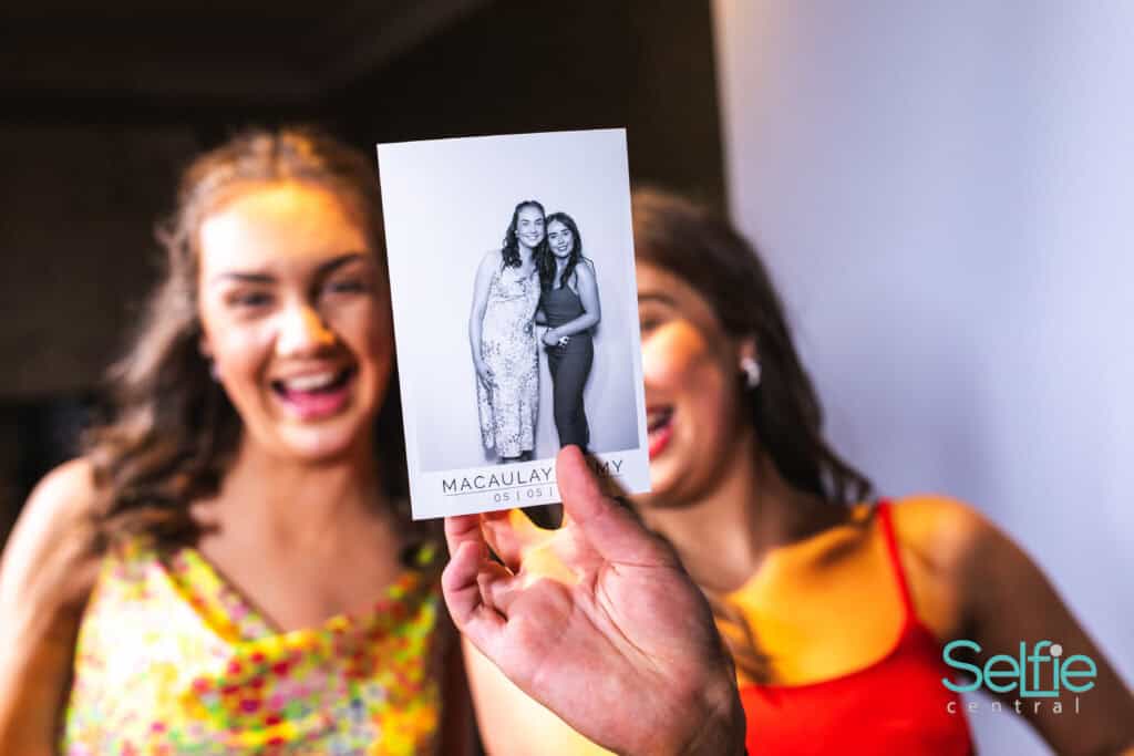 Two women smiling with a black-and-white photo in front of them at a photo booth.