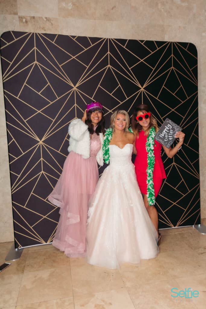 Three women at a photo booth, one in a wedding dress, celebrating at Selfie Central Auckland.