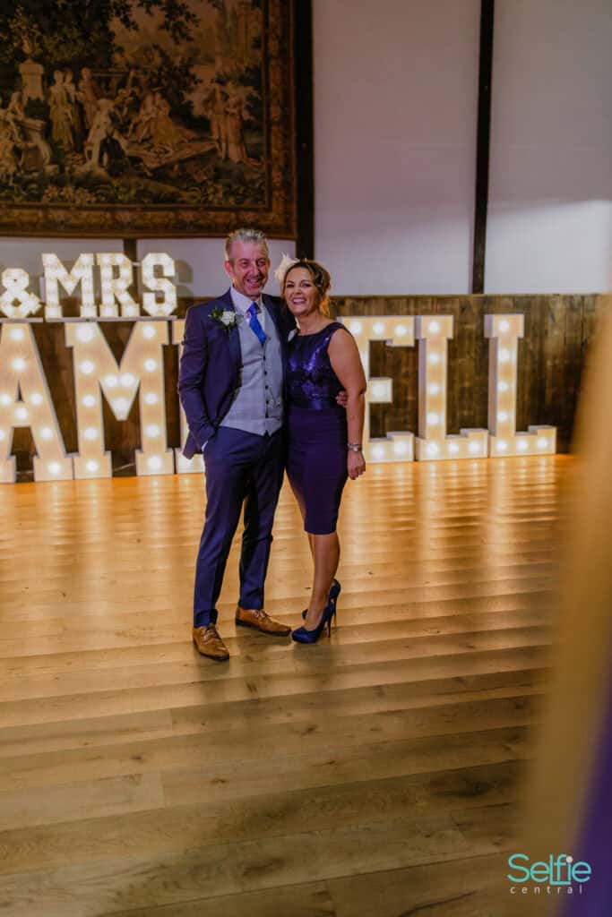 Happy wedding couple at Selfie Central photo booth with illuminated 'MR & MRS' sign.